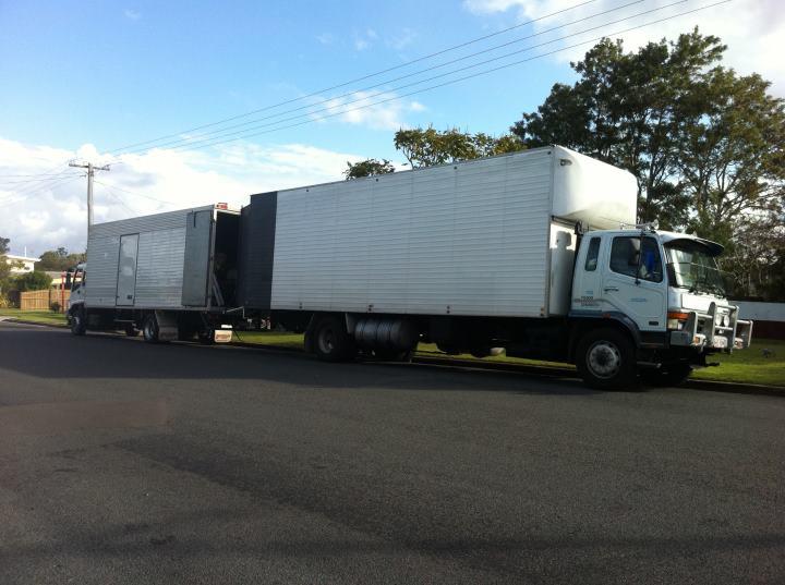 Removals truck towing a furniture trailer, parked on a suburban street