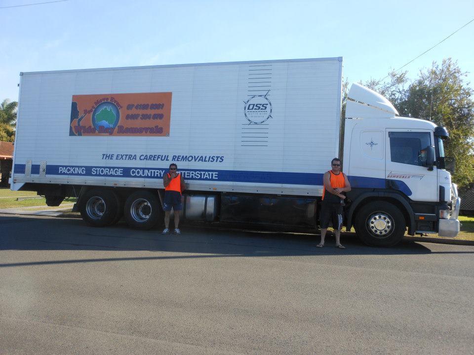 Two removalists in hi-vis standing beside a signwritten removals truck