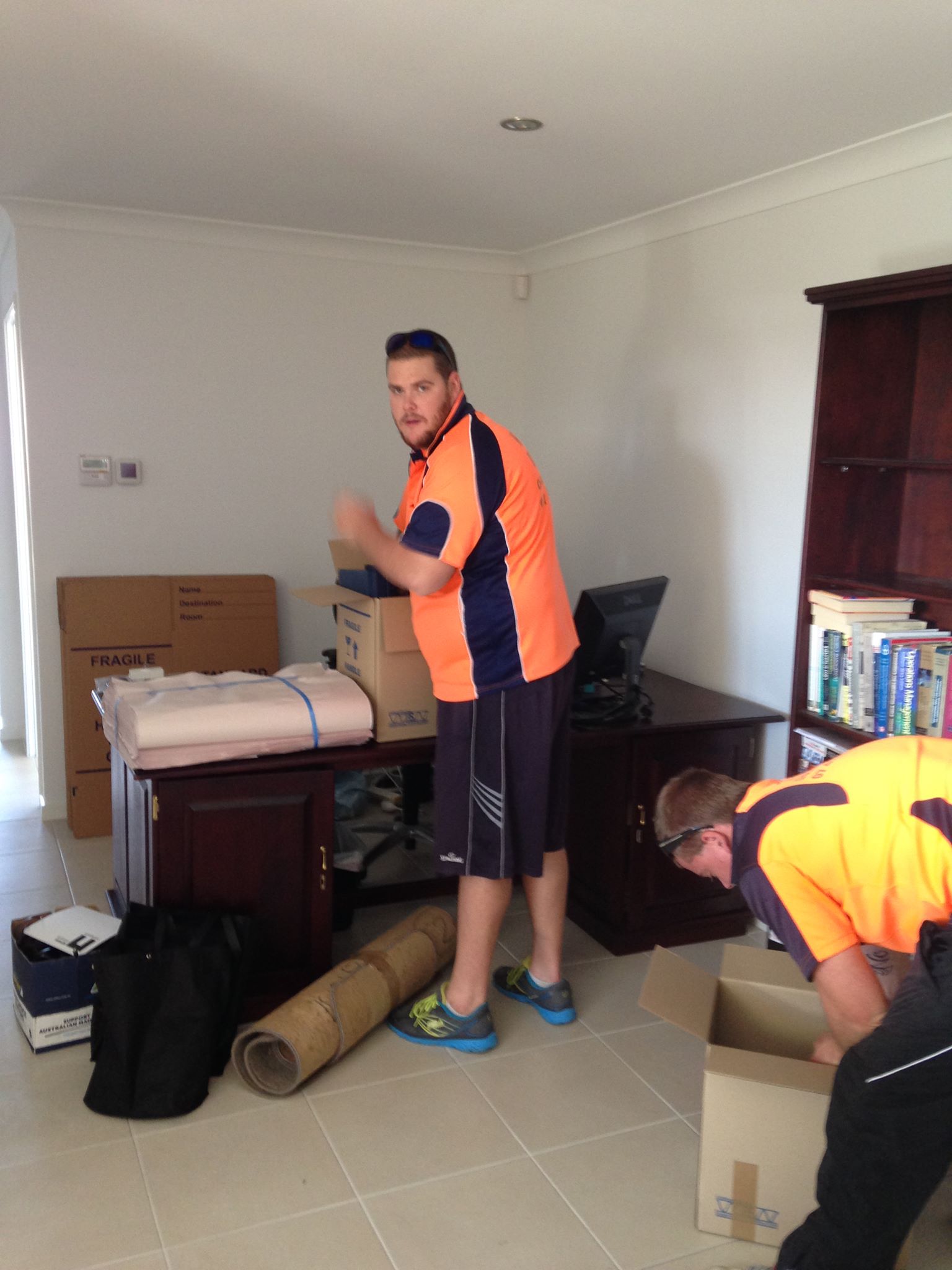Two removalists in hi-vis shirts packing boxes beside a timber desk