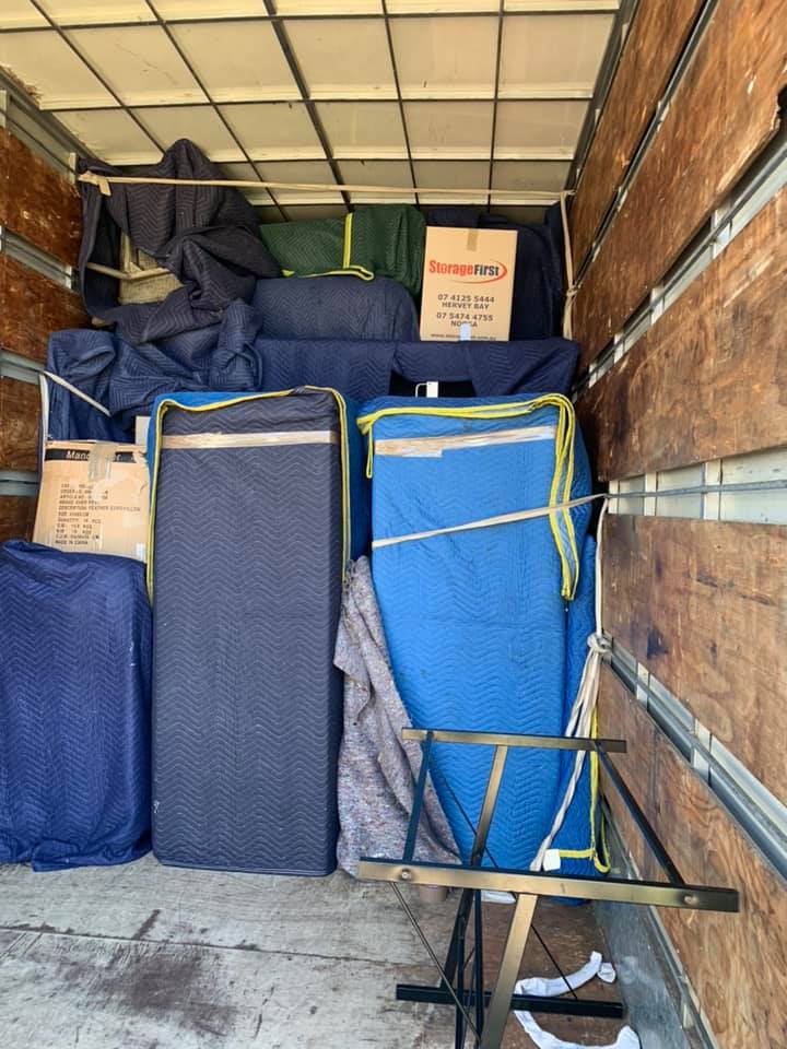 Mattresses and furniture wrapped in blue moving blankets inside a truck
